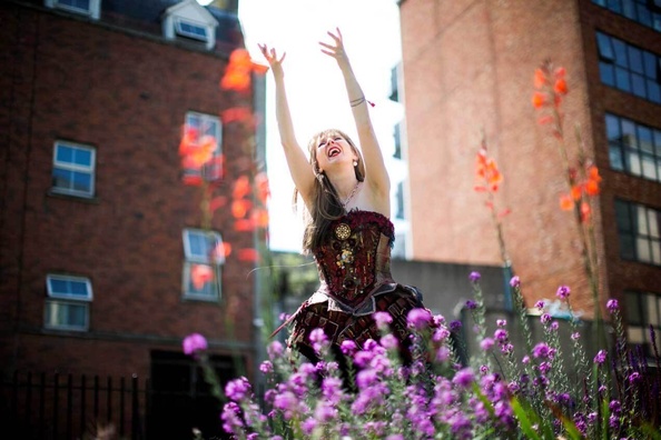 Opera perfomer with raised arms singing in-between flowers